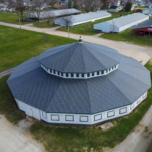 Aerial view of large round commercial building with gray shingled roof and cupola